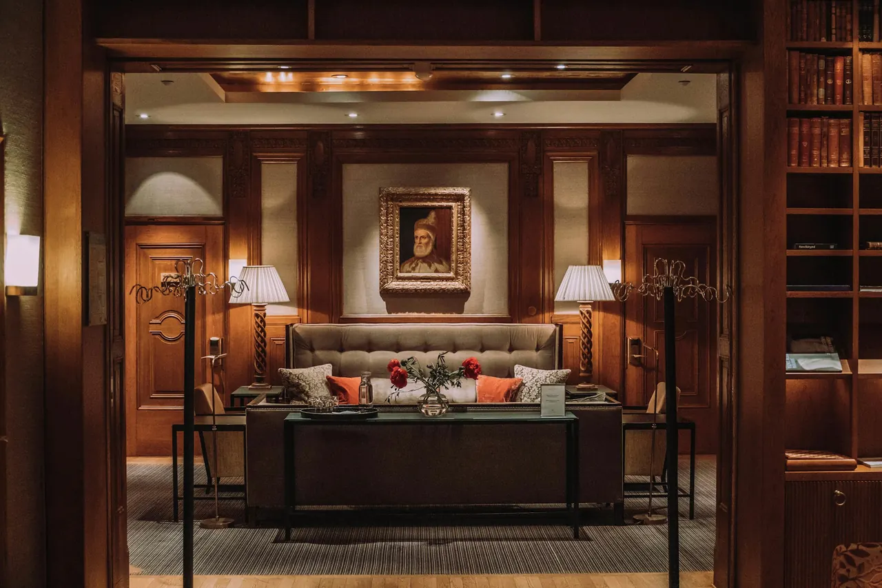 A wood-panelled hotel lounge with warm lamps, a framed portrait and a leather sofa