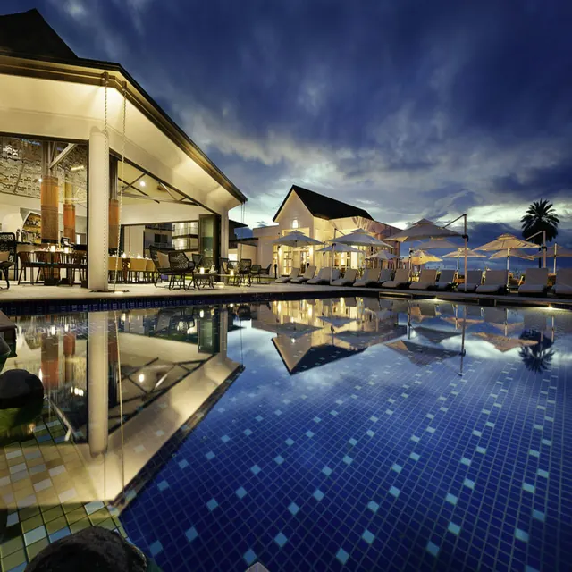 The hotel pool at dusk, with loungers and parasols reflected in the water