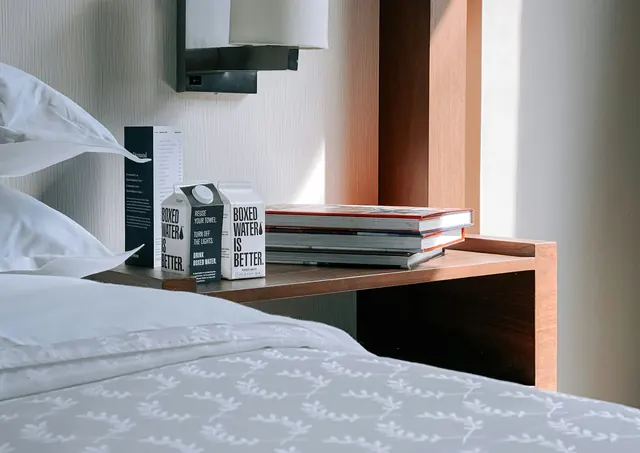 A bedside table with bottled water and books beside fresh hotel linens