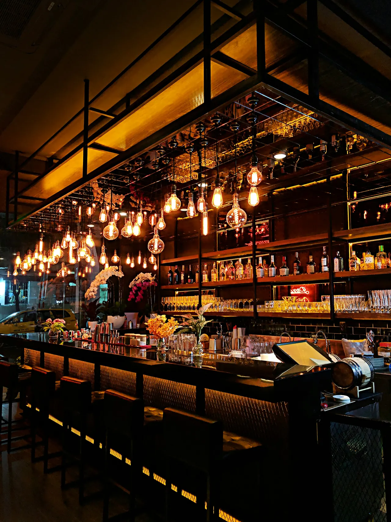 A bar glowing with hanging lights and shelves of bottles at night