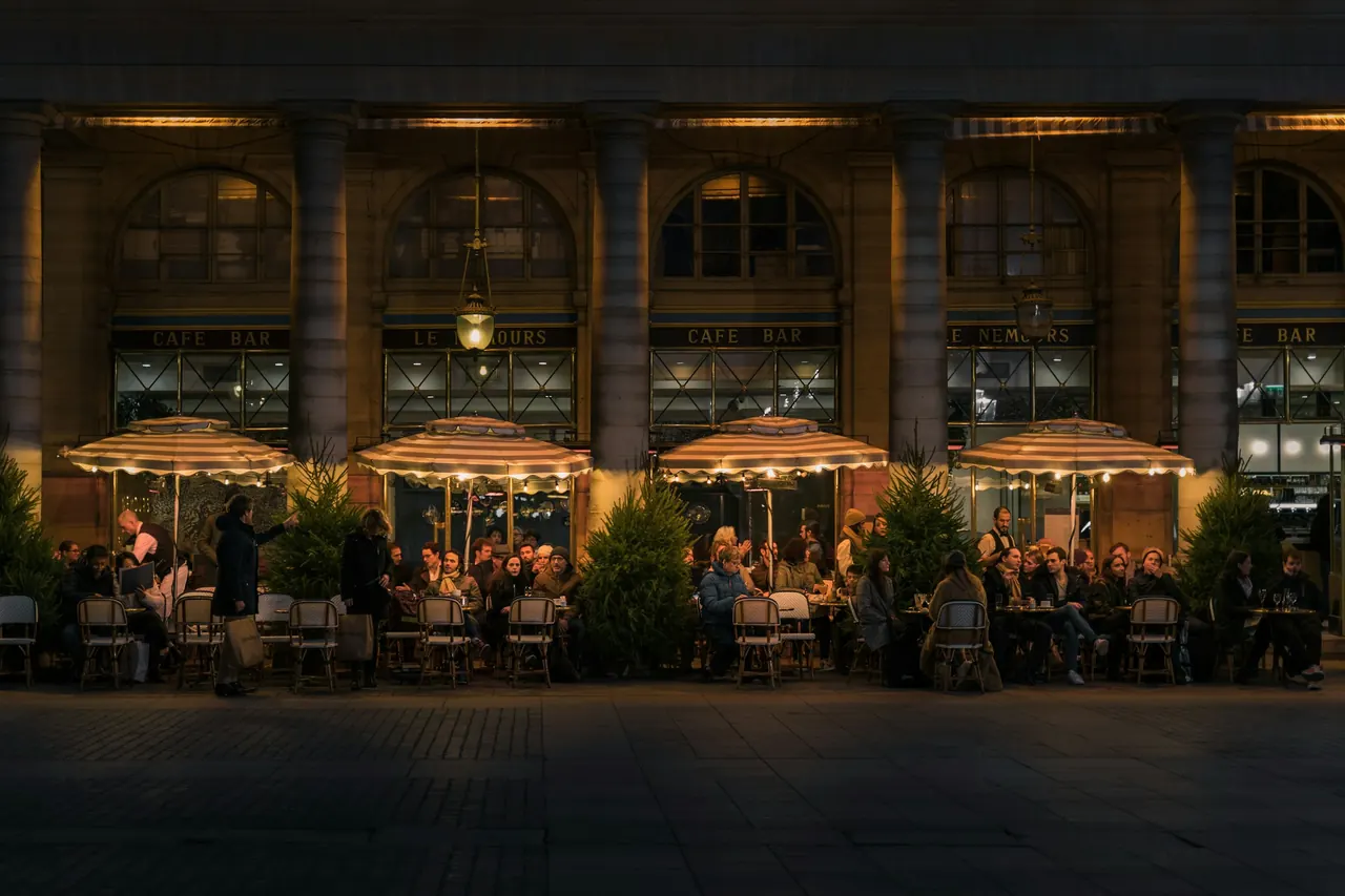 Outdoor restaurant terraces in a historic square, lit up in the evening