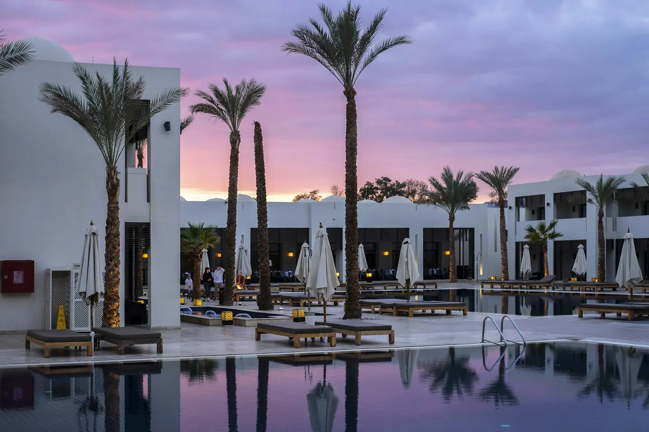 White hotel buildings and palm trees around a pool at dusk