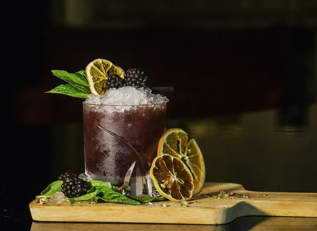 A dark cocktail garnished with dried citrus and berries